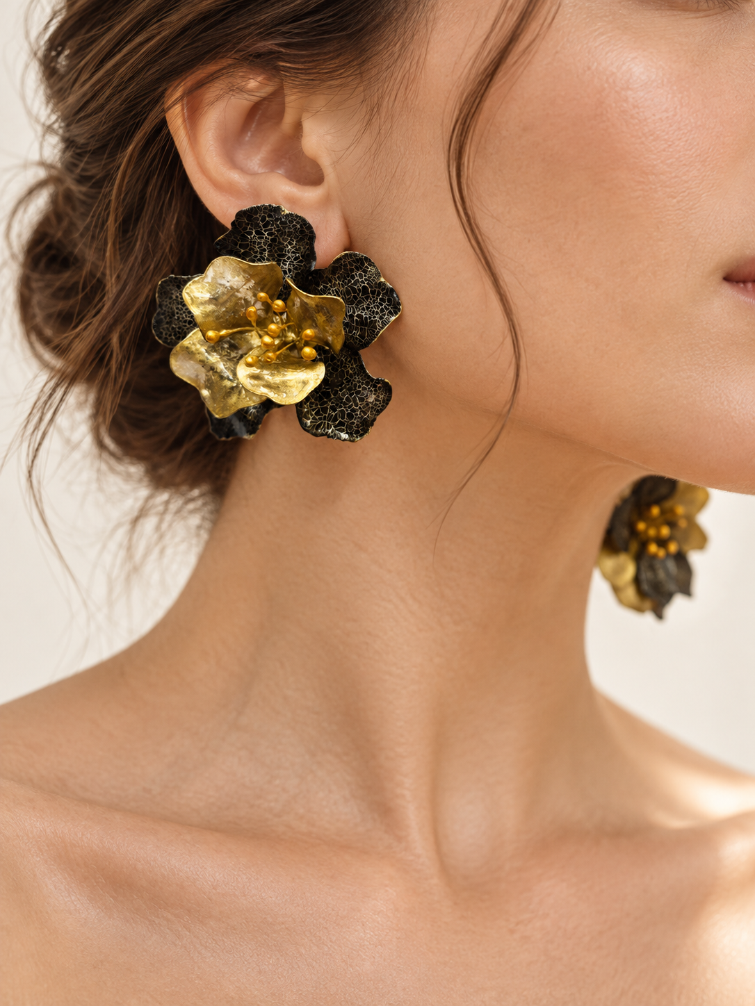 Black and antique-gold flower earrings worn at the ear