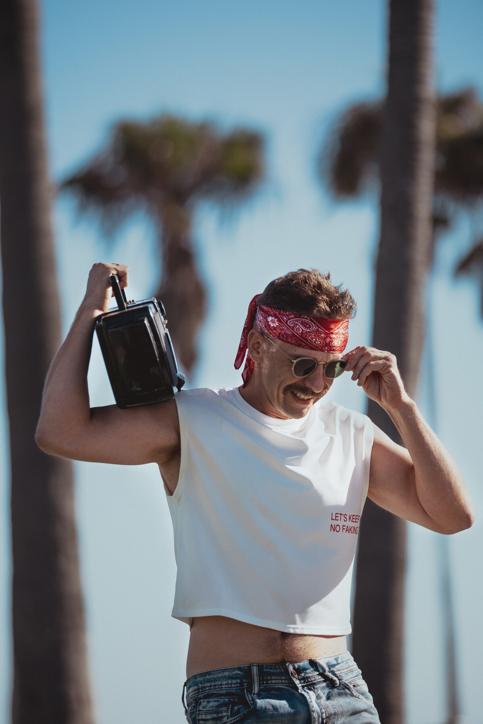 Man in bandana and sunglasses holding a vintage boombox over his shoulder